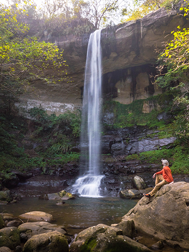 Hiker sitting on rock looking at Pipa Cave Waterfall