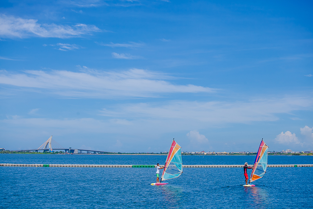 Two windsurfers on the blue lagoon of Dapeng Bay